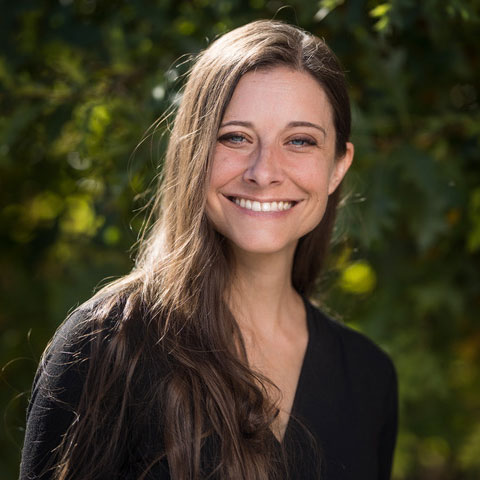 Photo of smiling white woman. The photo has trees in the background